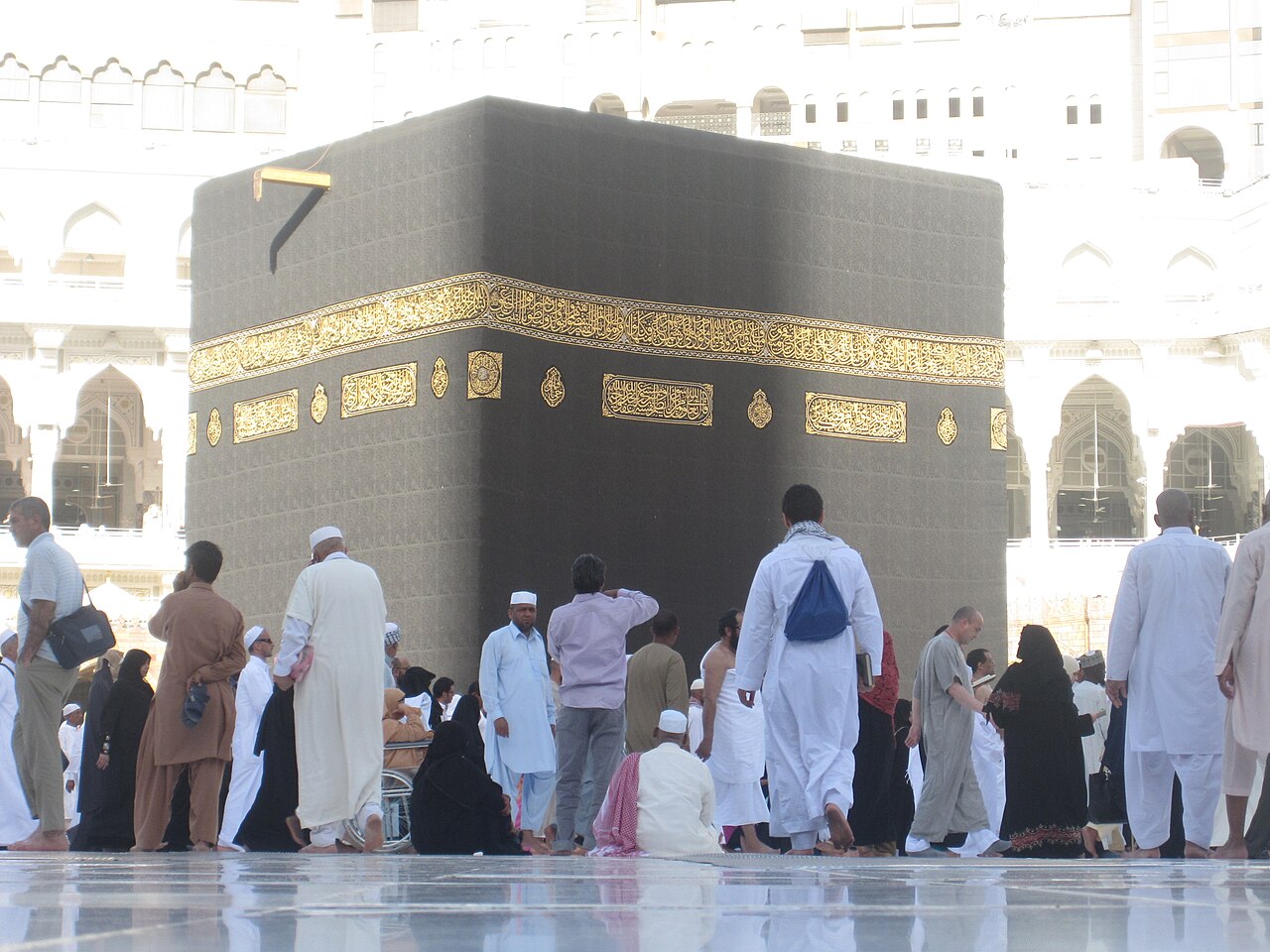 Ka'bah berkiswah hitam berhias kaligrafi emas, jemaah berjalan di sekitarnya